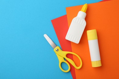 Glue, colorful paper and scissors on light blue background, flat lay. Space for text