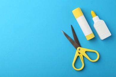 Photo of Different types of glue and scissors on light blue background, flat lay. Space for text