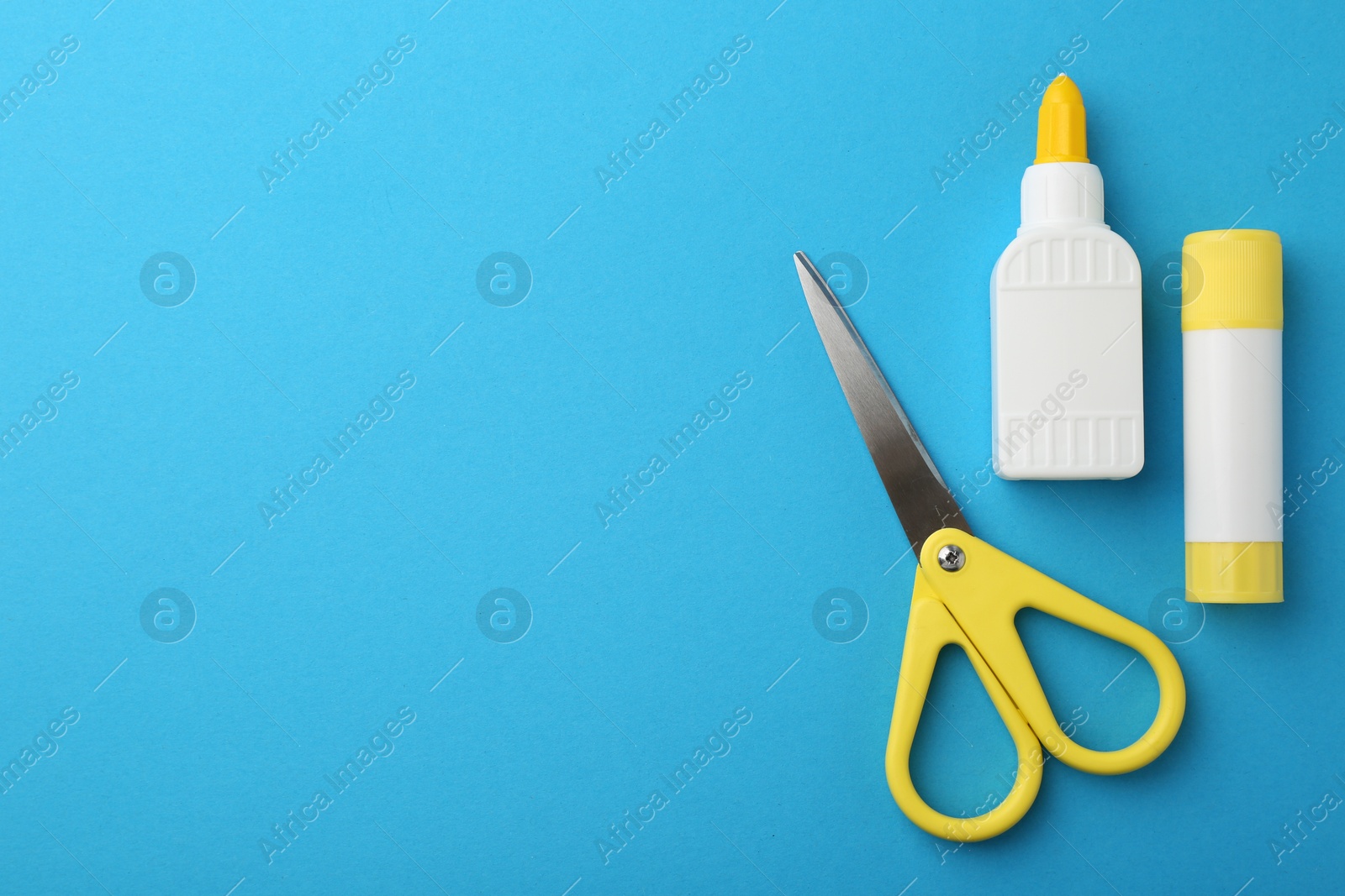 Photo of Different types of glue and scissors on light blue background, flat lay. Space for text