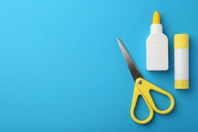 Different types of glue and scissors on light blue background, flat lay. Space for text