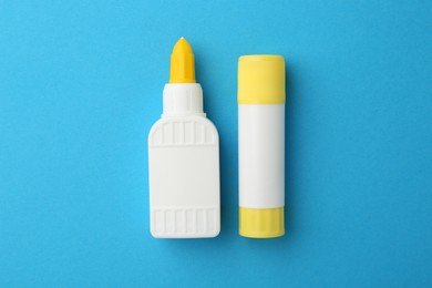 Different types of glue on light blue background, flat lay