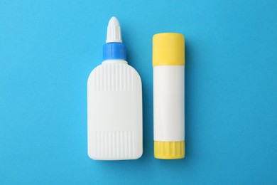 Different types of glue on light blue background, flat lay