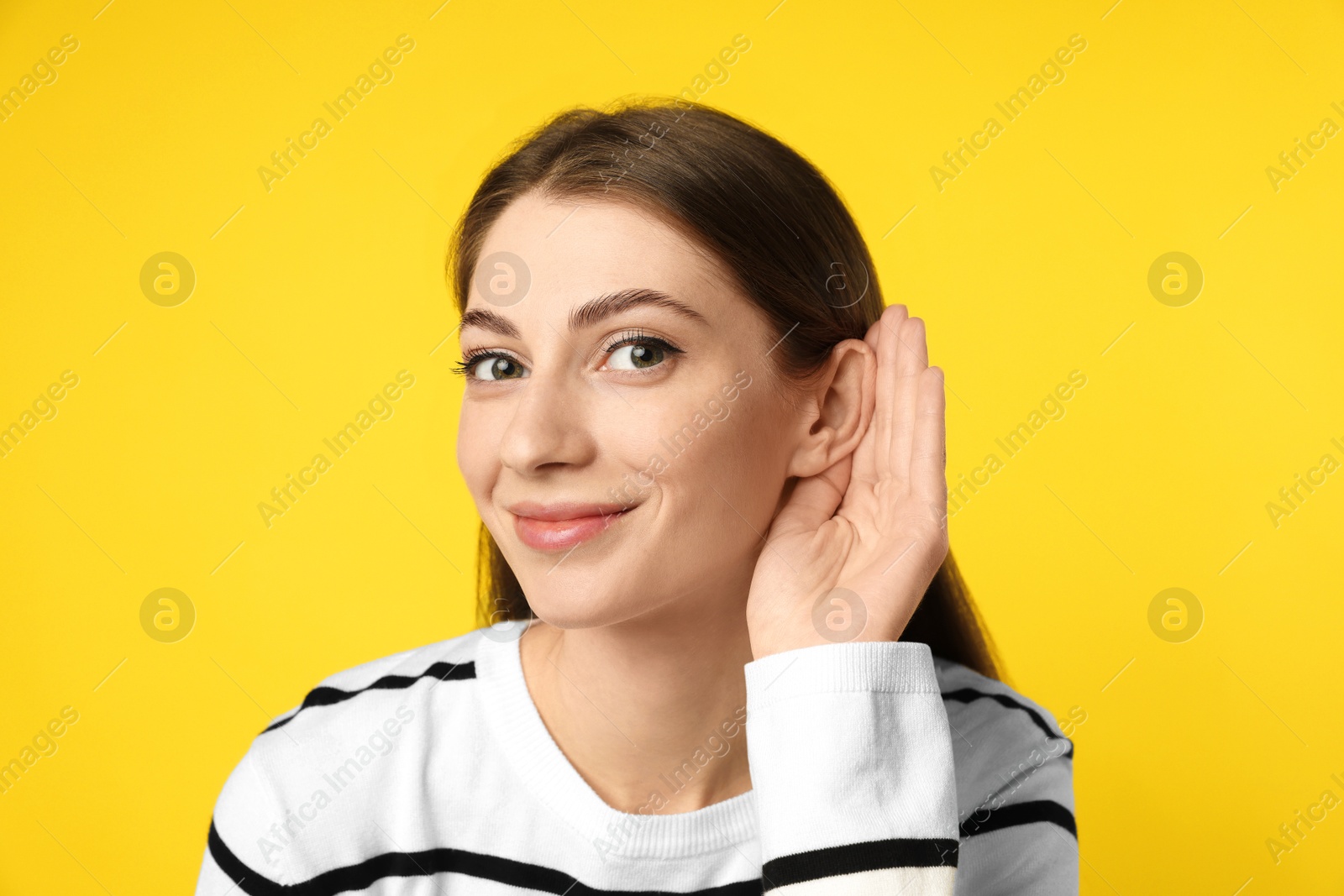 Photo of Woman showing hand to ear gesture on yellow background