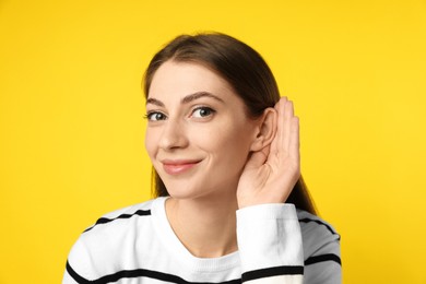 Woman showing hand to ear gesture on yellow background