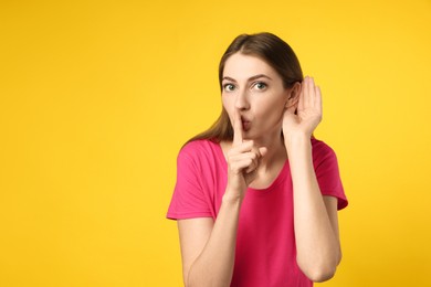 Woman showing hand to ear gesture on yellow background, space for text