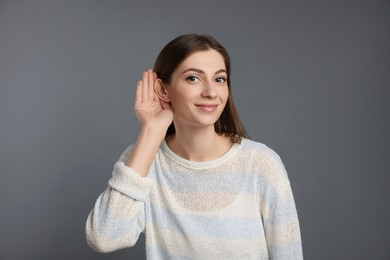 Woman showing hand to ear gesture on grey background