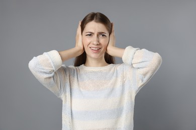 Woman covering her ears on grey background