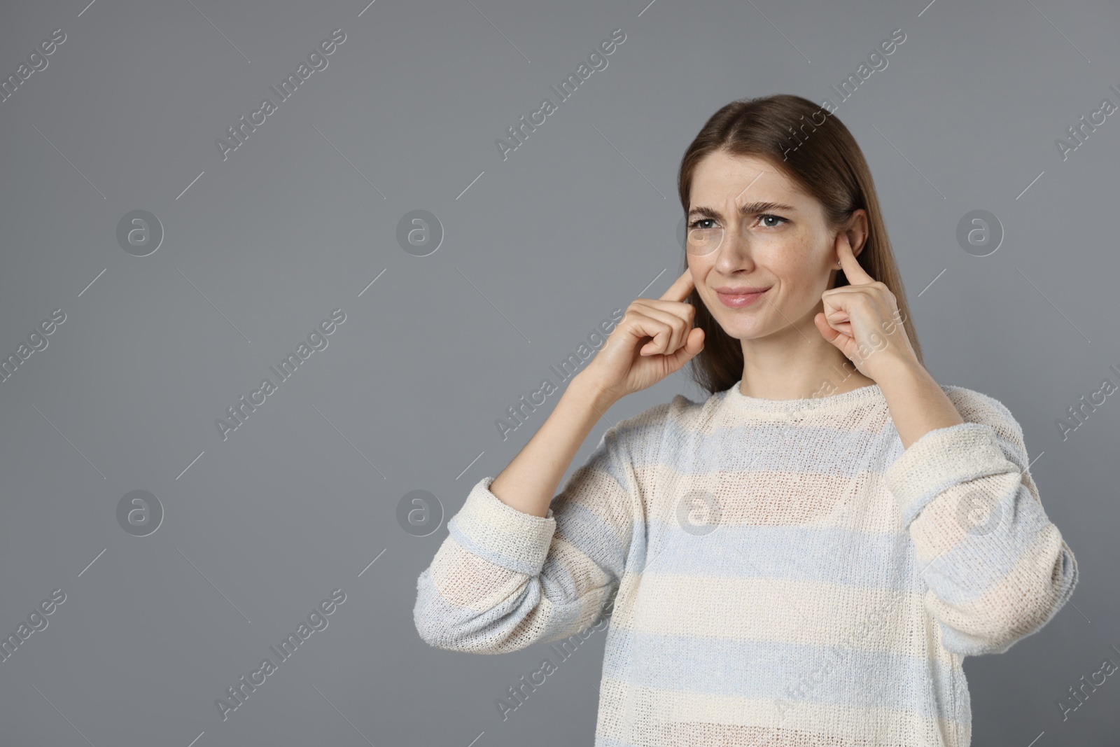 Photo of Woman covering her ears with fingers on grey background, space for text