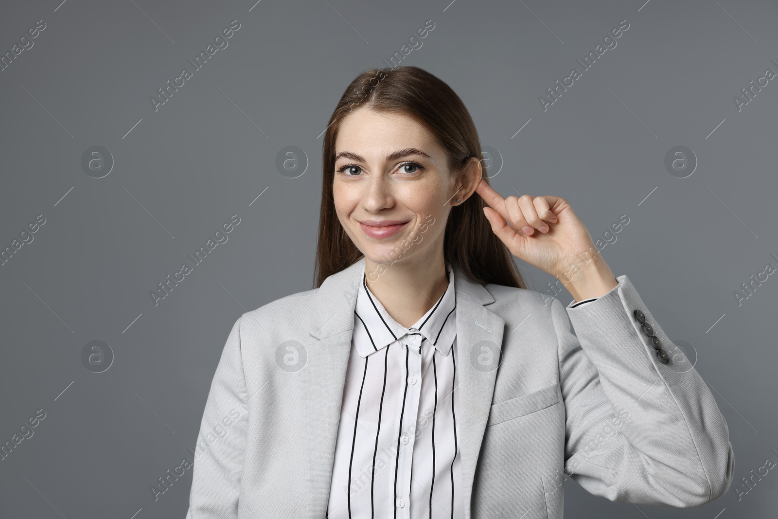 Photo of Woman showing hand to ear gesture on grey background