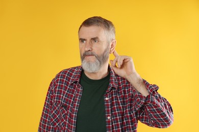 Senior man showing hand to ear gesture on orange background