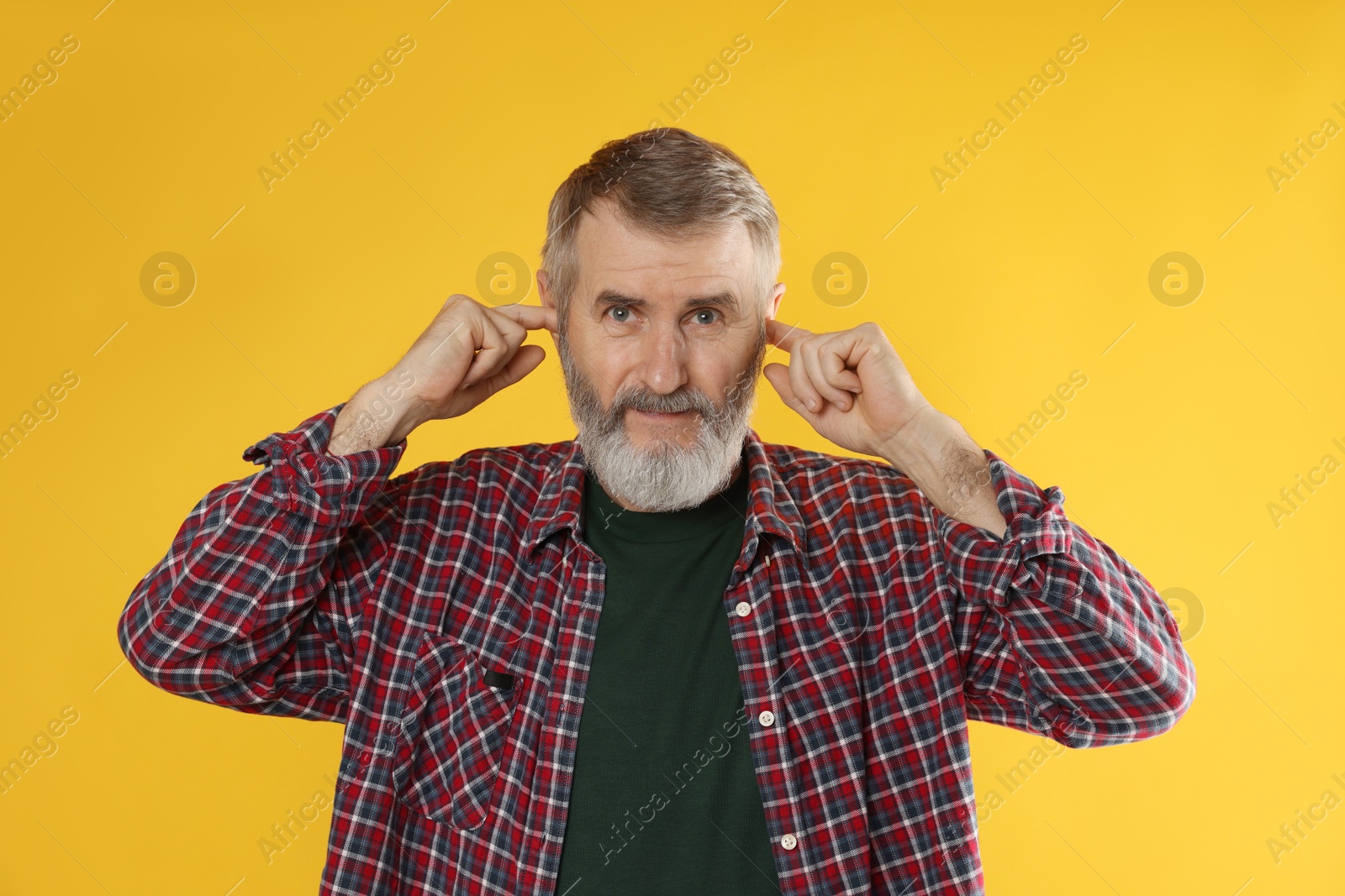 Photo of Senior man covering his ears with fingers on orange background