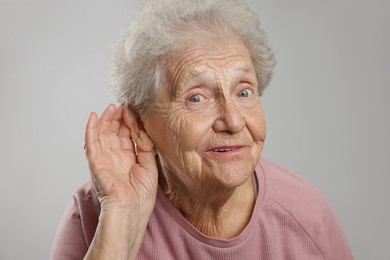 Photo of Senior woman showing hand to ear gesture on grey background