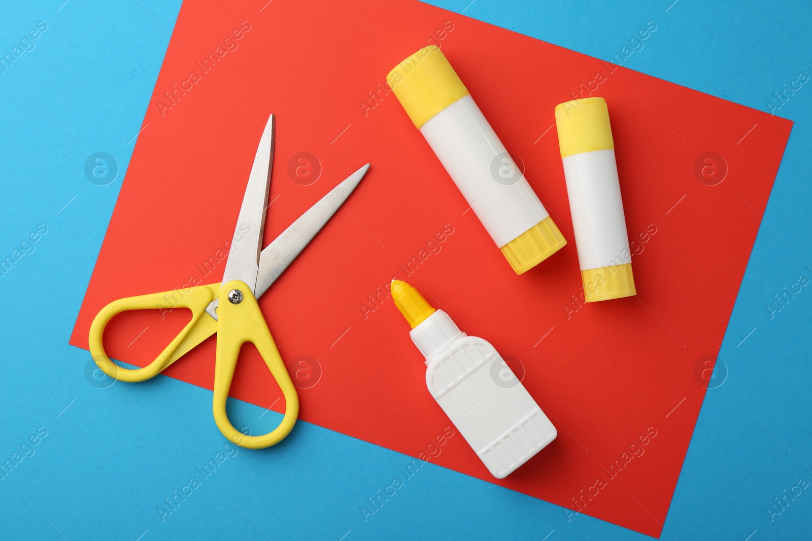 Photo of Glue, colorful paper and scissors on light blue background, flat lay