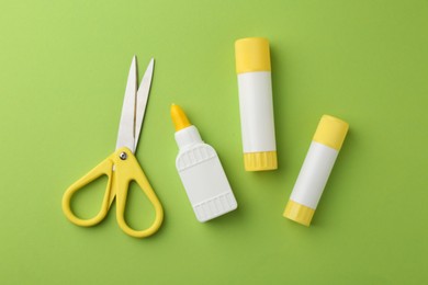 Photo of Different types of glue and scissors on green background, flat lay