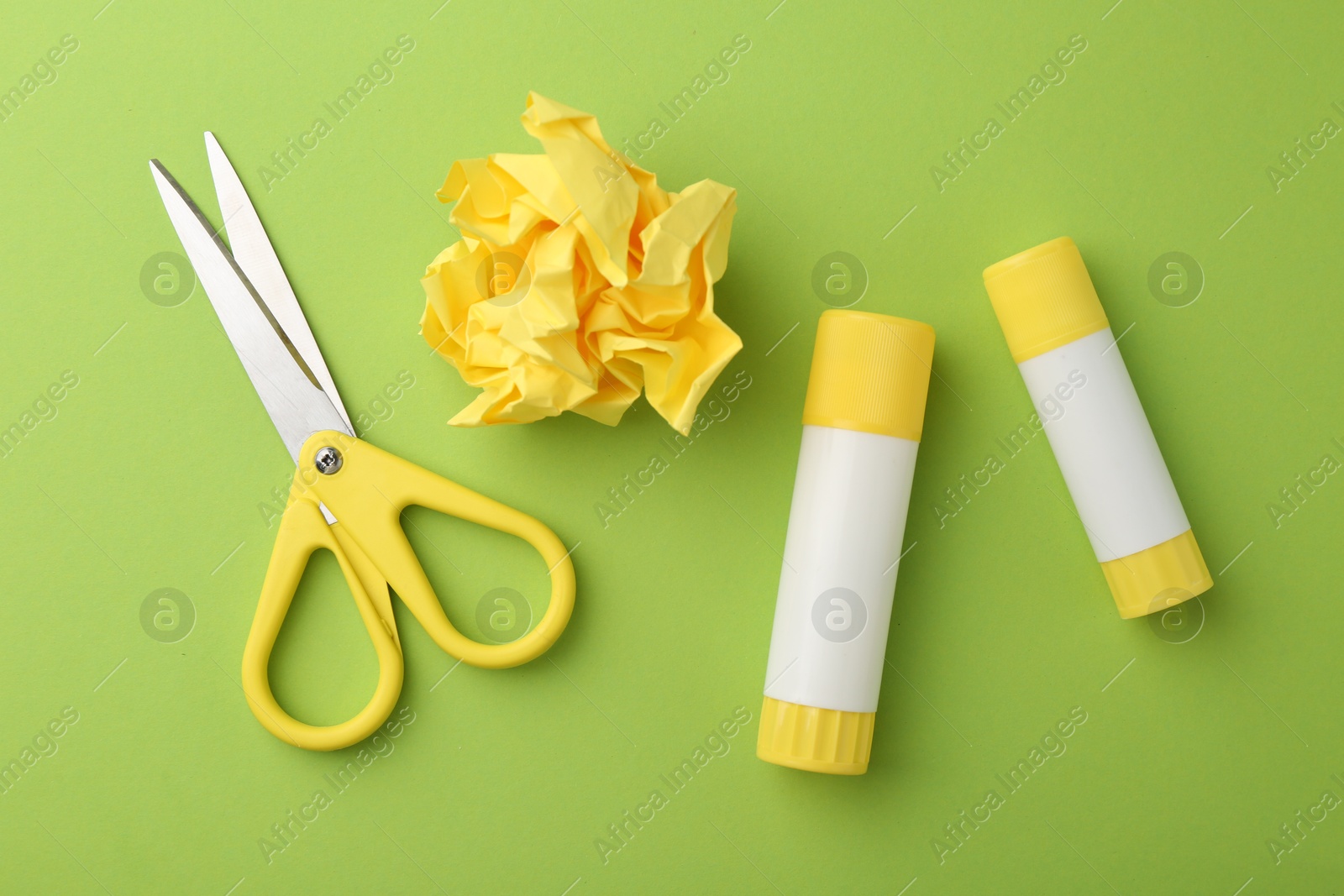 Photo of Glue, crumpled paper and scissors on green background, flat lay