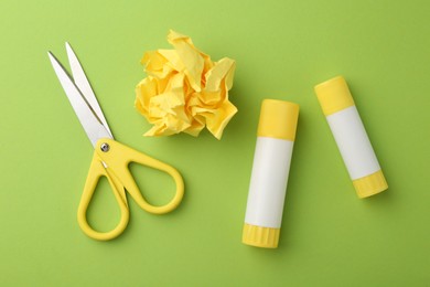 Photo of Glue, crumpled paper and scissors on green background, flat lay