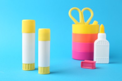 Photo of Different types of glue and colorful holder on light blue background, closeup