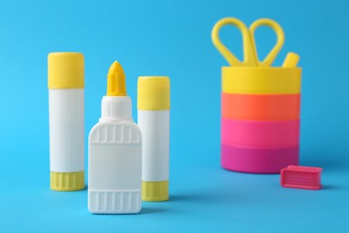 Photo of Different types of glue and colorful holder on light blue background, closeup