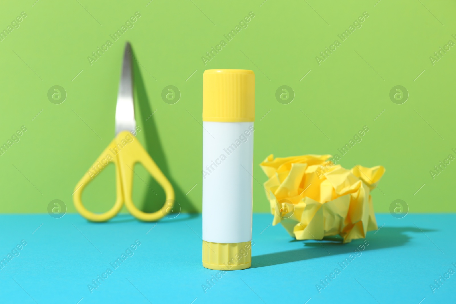 Photo of Glue, crumpled paper and scissors on color background, closeup