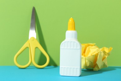 Photo of Bottle of glue, crumpled paper and scissors on color background, closeup