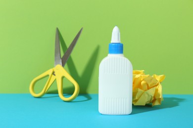 Photo of Bottle of glue, crumpled paper and scissors on color background, closeup