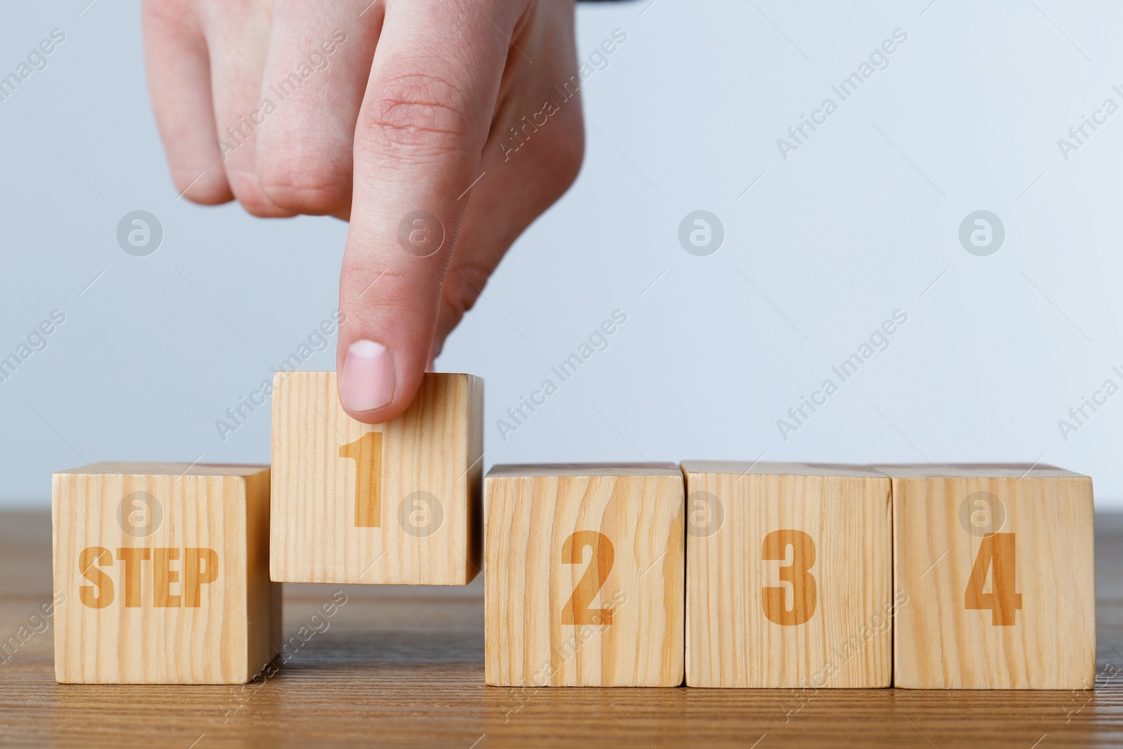 Image of Man putting wooden cube with number 1 between other ones with word Step and number 2 onto table, closeup. Step-by-step concept