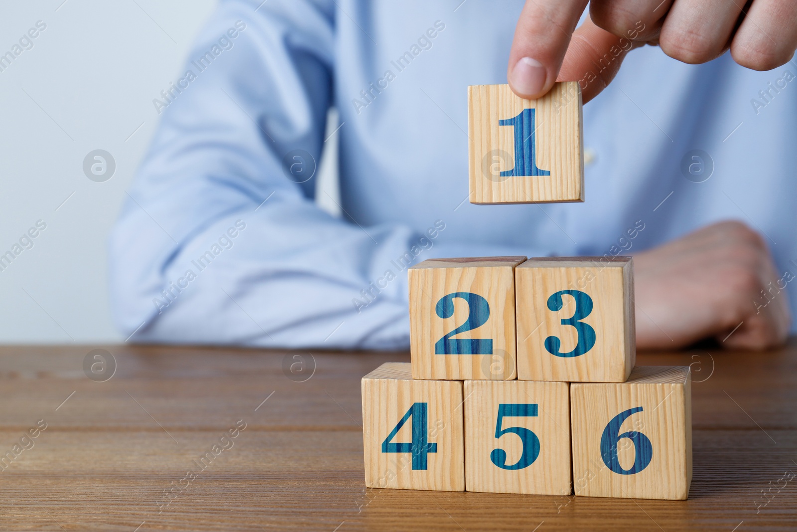 Image of Man building pyramid of numbered cubes at wooden table, closeup. Step-by-step concept