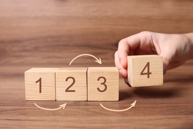 Image of Man putting cube with digit 4 to row of other numbered ones onto wooden table, closeup. Step-by-step concept