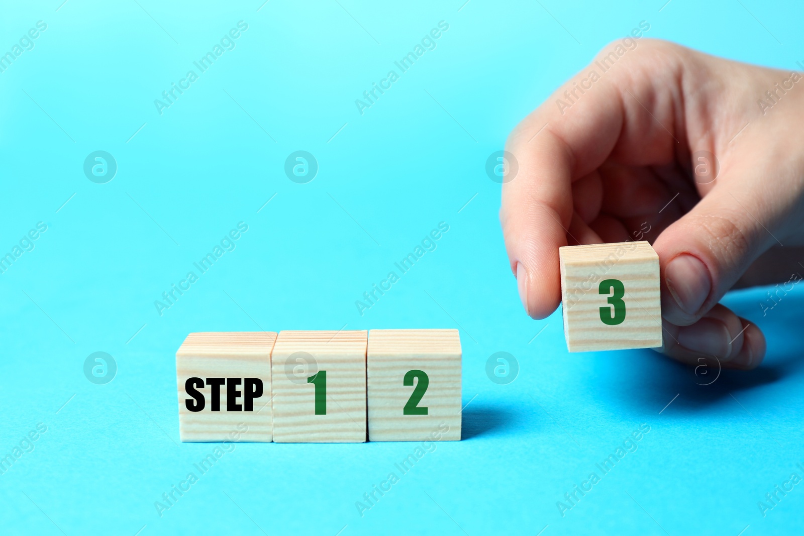 Image of Woman putting wooden cube with digit 3 to row of other numbered ones on light blue background, closeup. Step-by-step concept