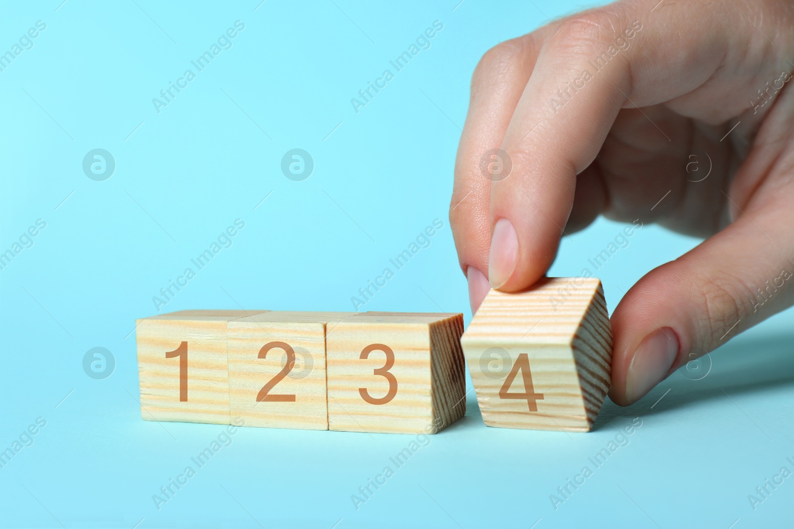 Image of Man putting wooden cube with digit 4 to row of other numbered ones on light blue background, closeup. Step-by-step concept