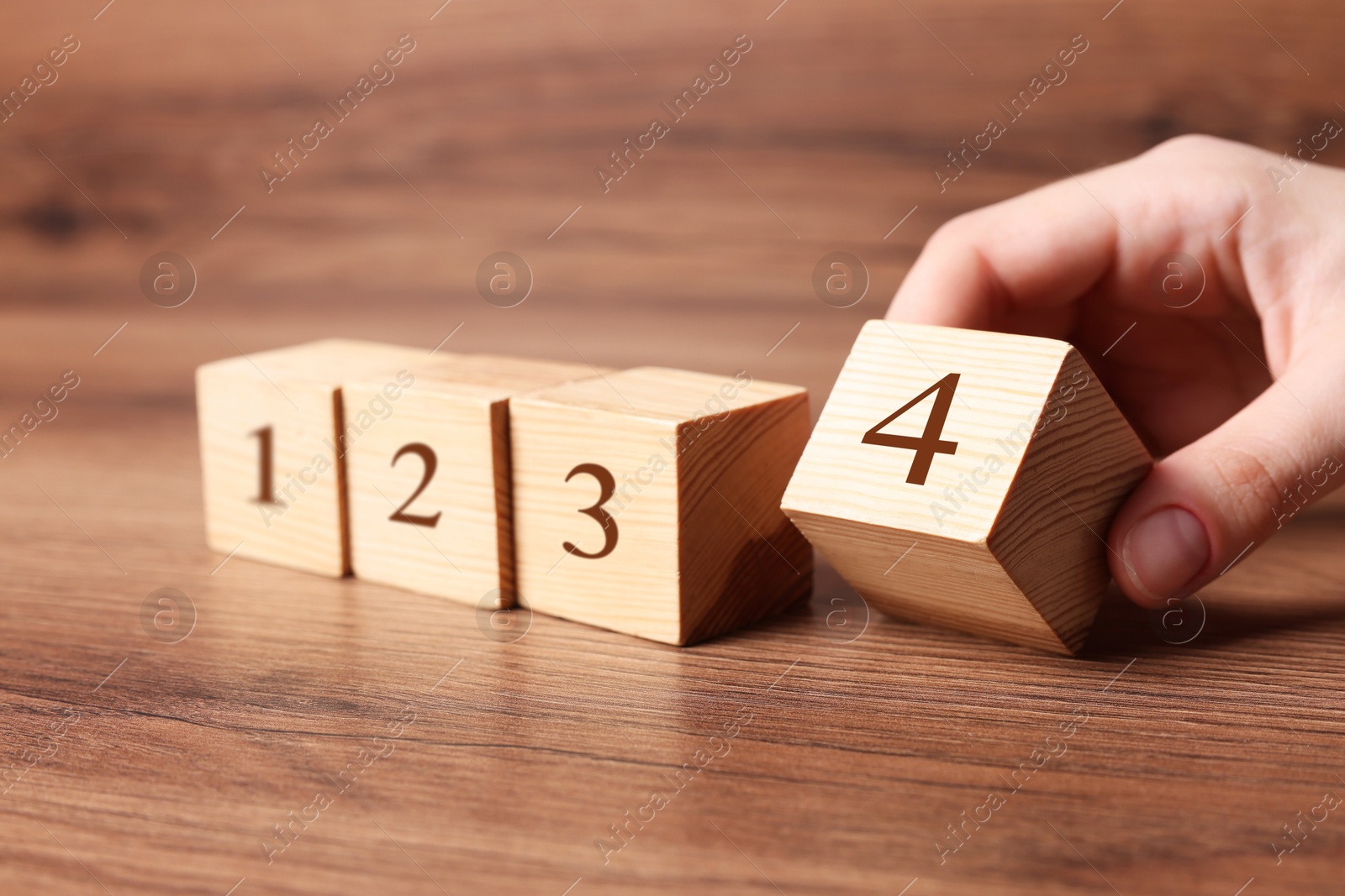 Image of Woman putting cube with digit 4 to row of other numbered ones onto wooden table, closeup. Step-by-step concept