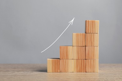 Image of Stair of wooden cubes and arrow on grey background. Step-by-step concept