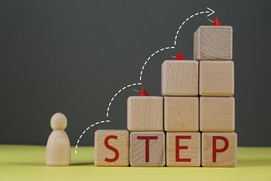 Image of Human figure in front of wooden cubes stair with pins and word Step on yellow table. Arrow showing direction. Step-by-step concept