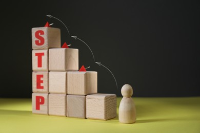 Image of Human figure in front of wooden cubes stair with pins and word Step on yellow table. Arrows showing direction. Step-by-step concept