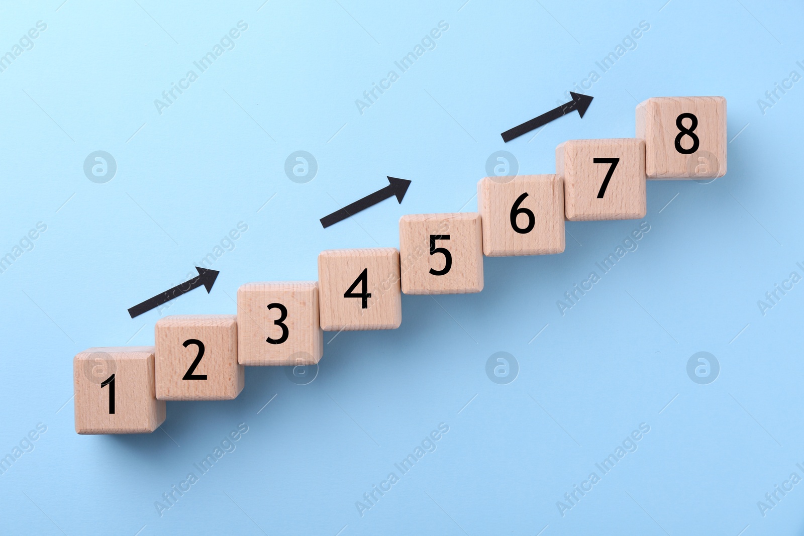 Image of Wooden numbered cubes and arrows on light blue background, top view. Step-by-step concept