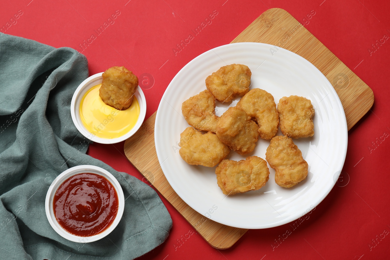 Photo of Delicious chicken nuggets and sauces on red background, flat lay