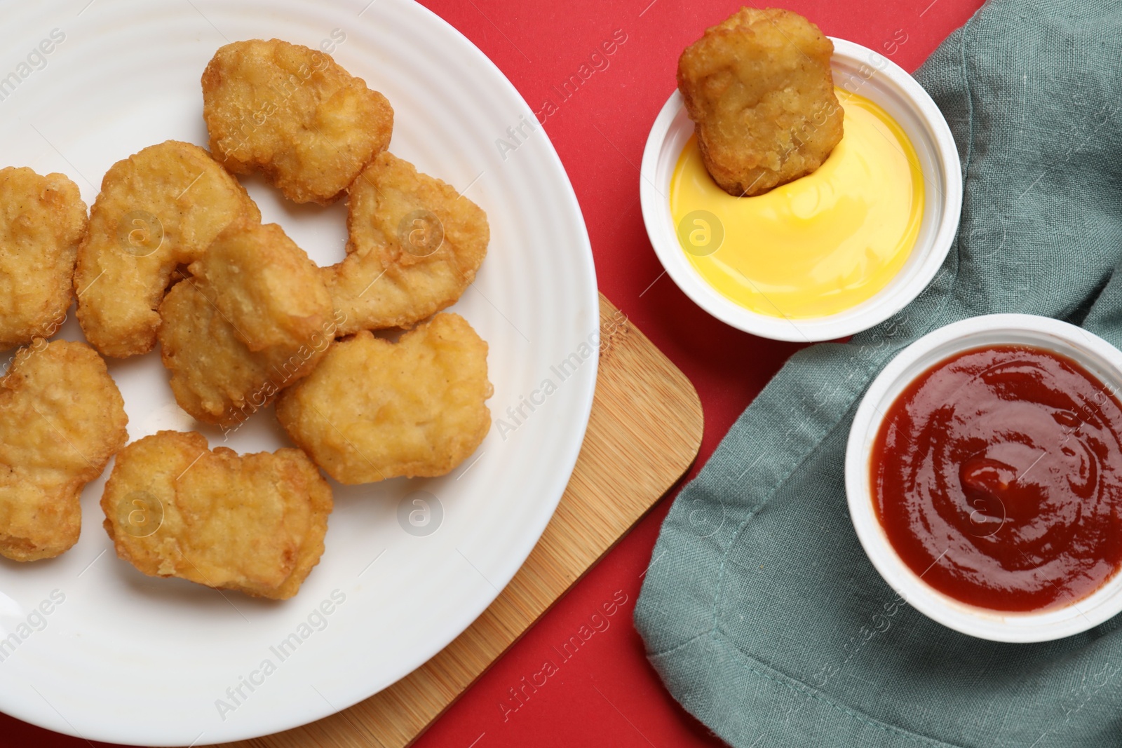 Photo of Delicious chicken nuggets and sauces on red background, flat lay