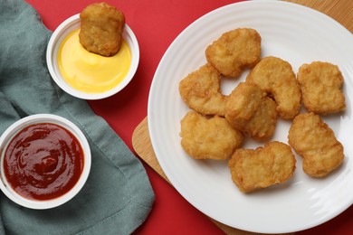 Photo of Delicious chicken nuggets and sauces on red background, flat lay