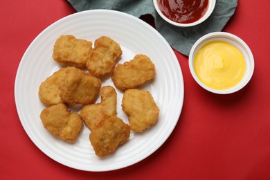 Photo of Delicious chicken nuggets and sauces on red background, flat lay