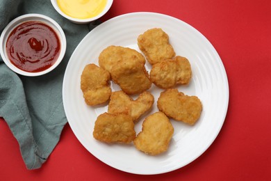 Photo of Delicious chicken nuggets and sauces on red background, flat lay