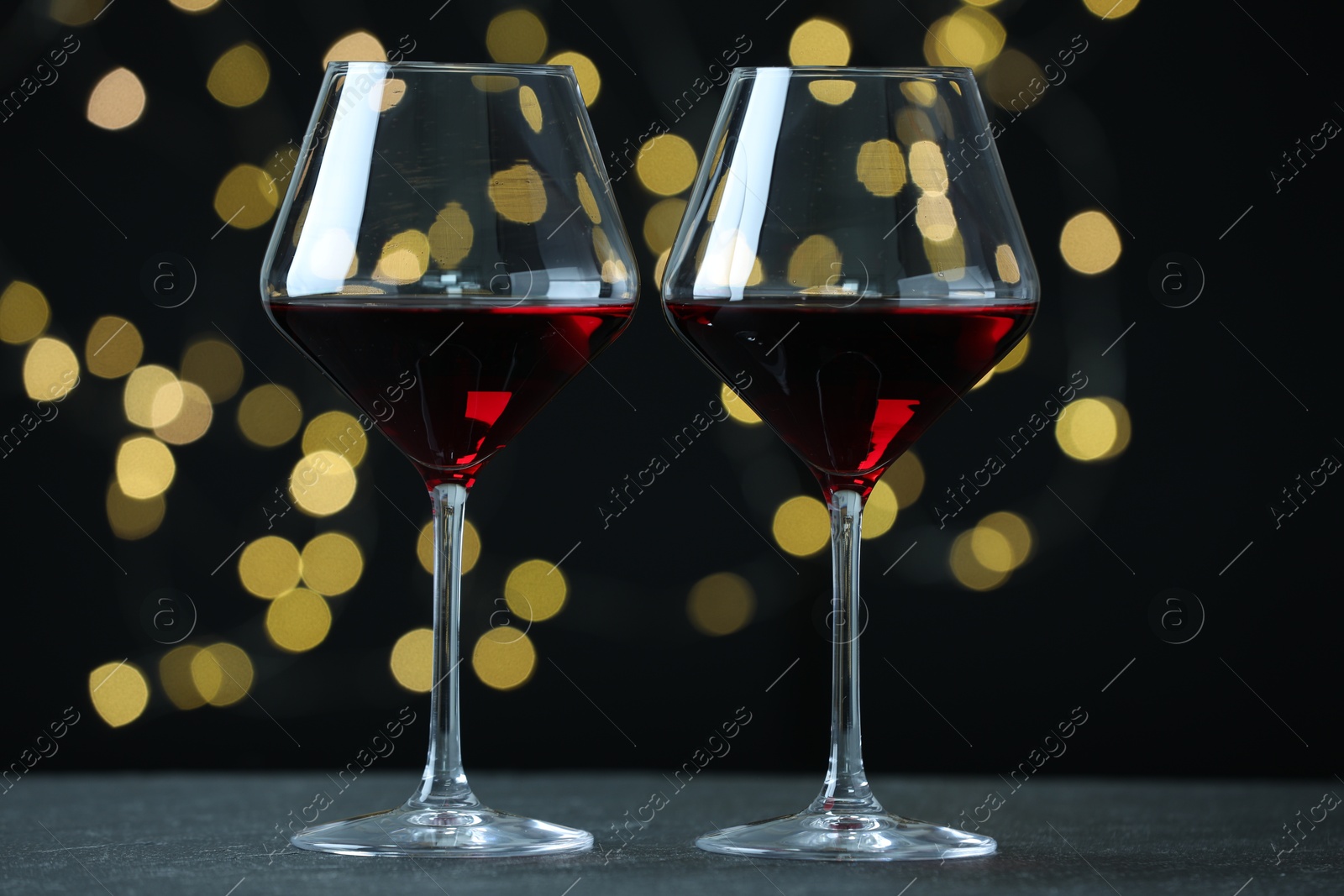 Photo of Glasses of luxury red wine on table against blurred lights. Bokeh effect