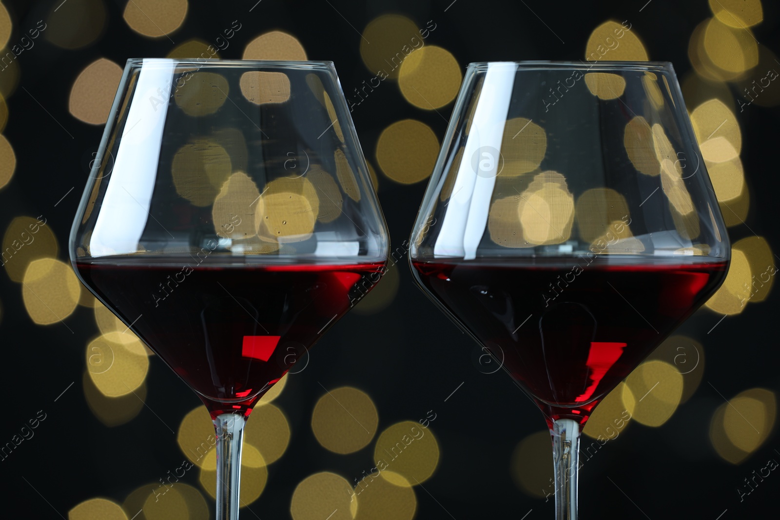 Photo of Glasses of luxury red wine against blurred lights, closeup. Bokeh effect