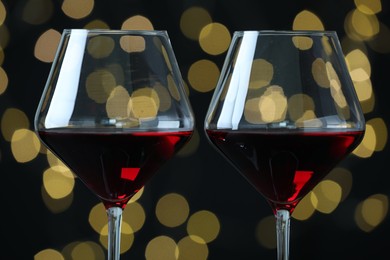 Glasses of luxury red wine against blurred lights, closeup. Bokeh effect