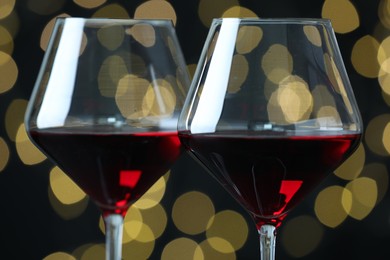 Photo of Glasses of luxury red wine against blurred lights, closeup. Bokeh effect