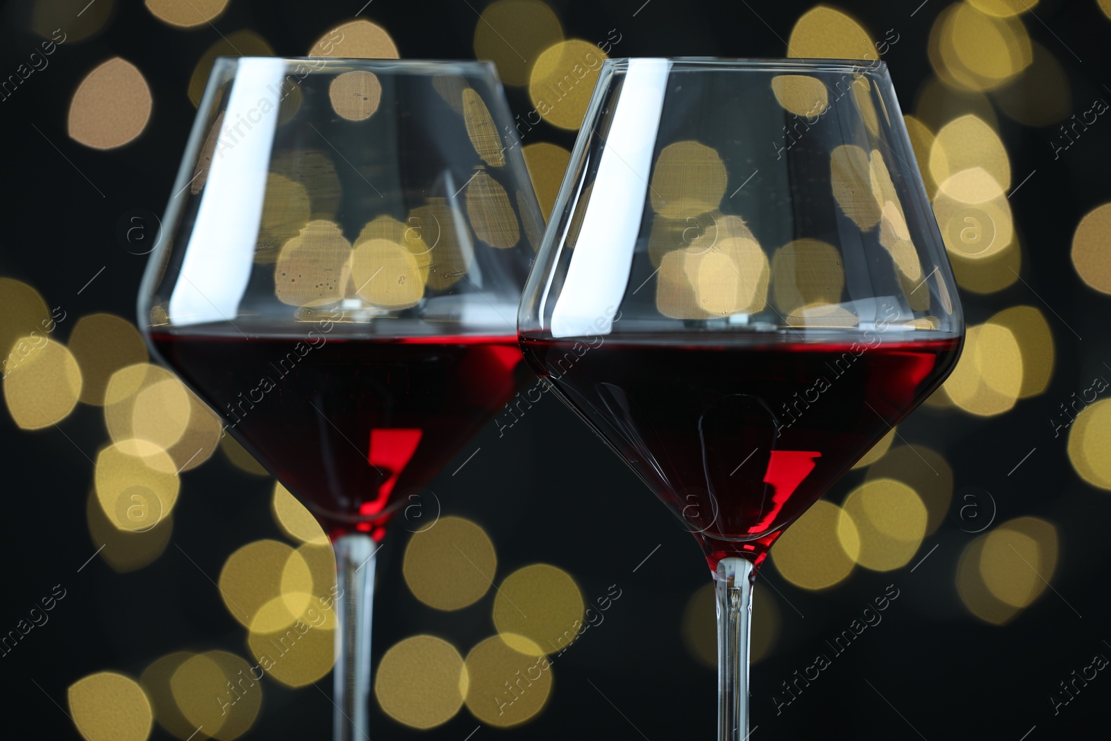 Photo of Glasses of luxury red wine against blurred lights, closeup. Bokeh effect