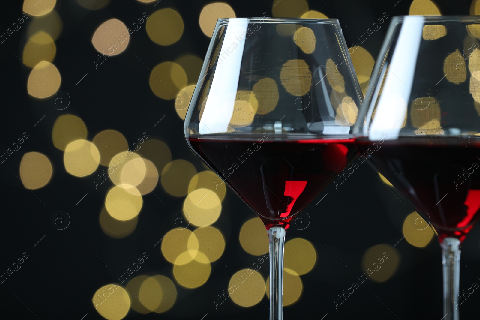 Photo of Glasses of luxury red wine against blurred lights, closeup. Bokeh effect