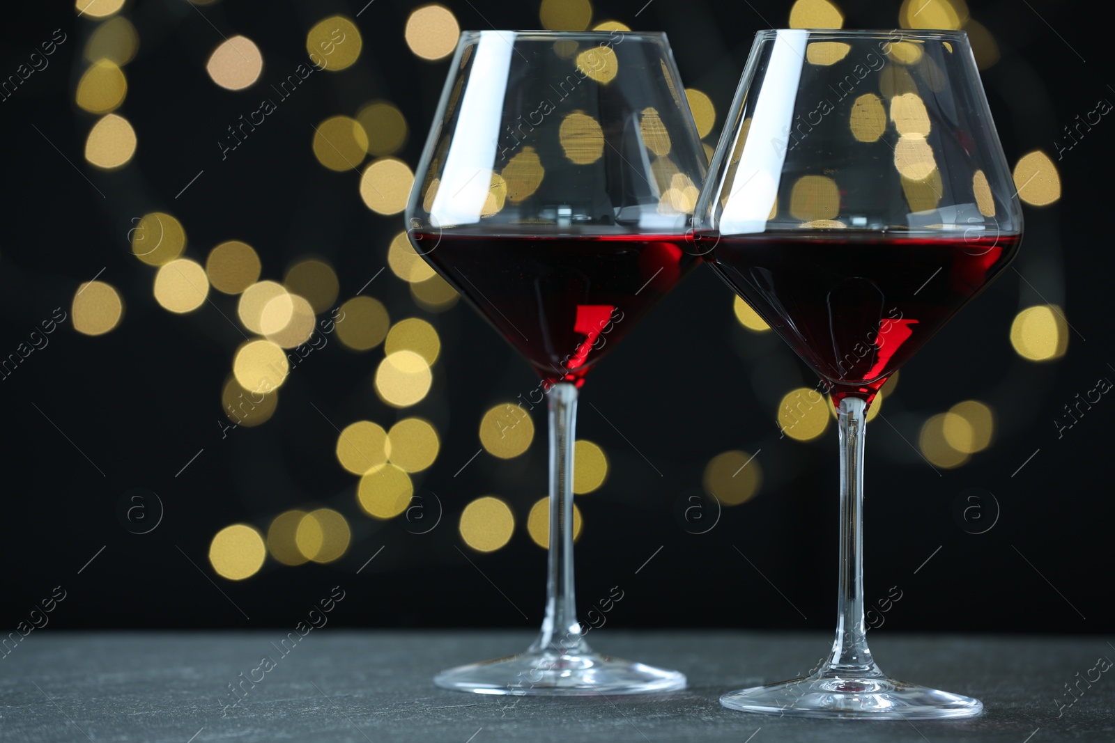 Photo of Glasses of luxury red wine on table against blurred lights. Bokeh effect