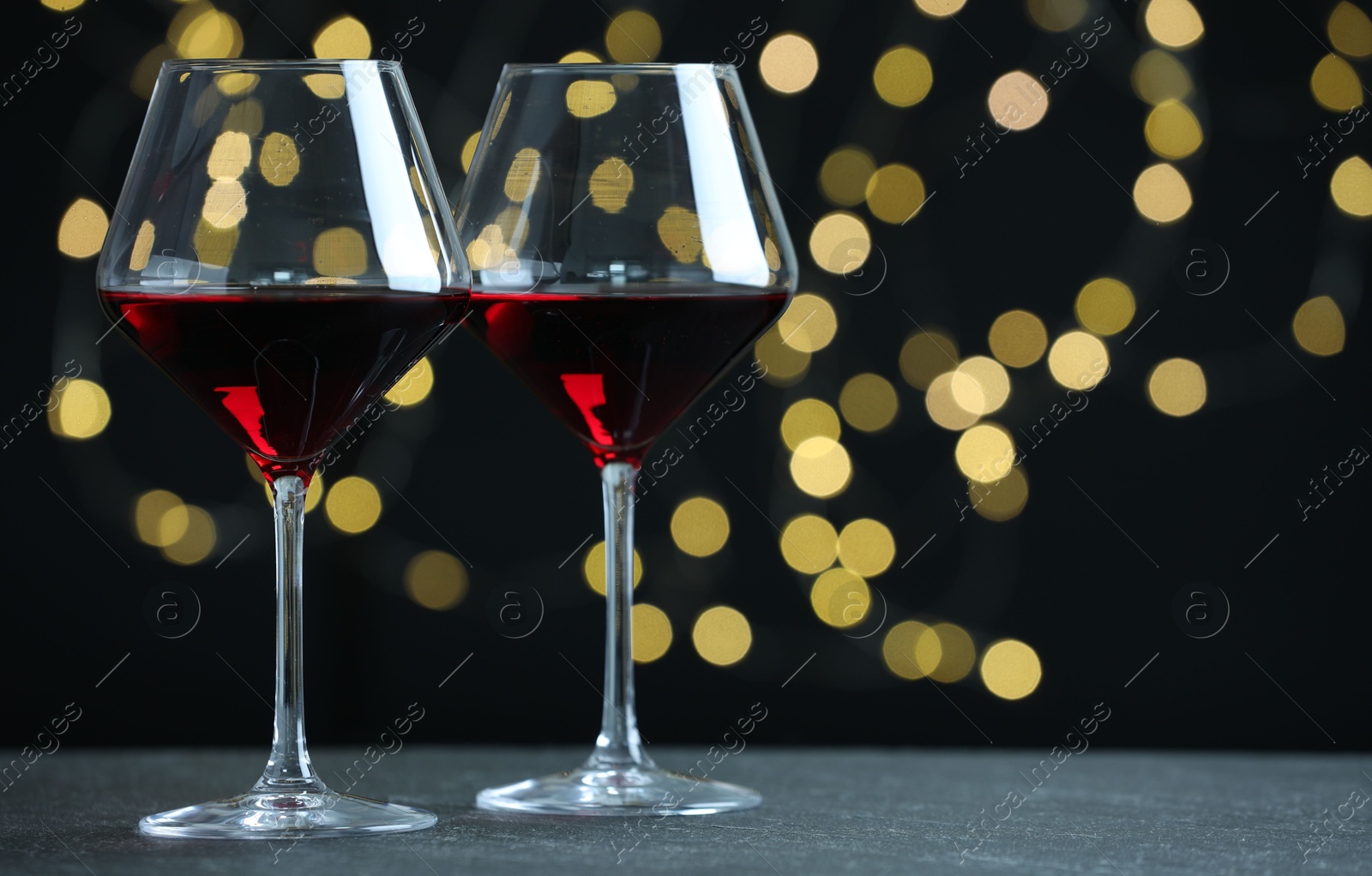 Photo of Glasses of luxury red wine on table against blurred lights. Bokeh effect