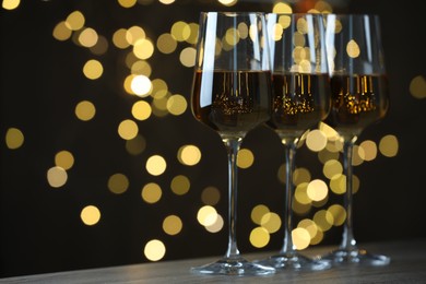 Photo of Glasses of luxury white wine on table against blurred lights, bokeh effect. Space for text