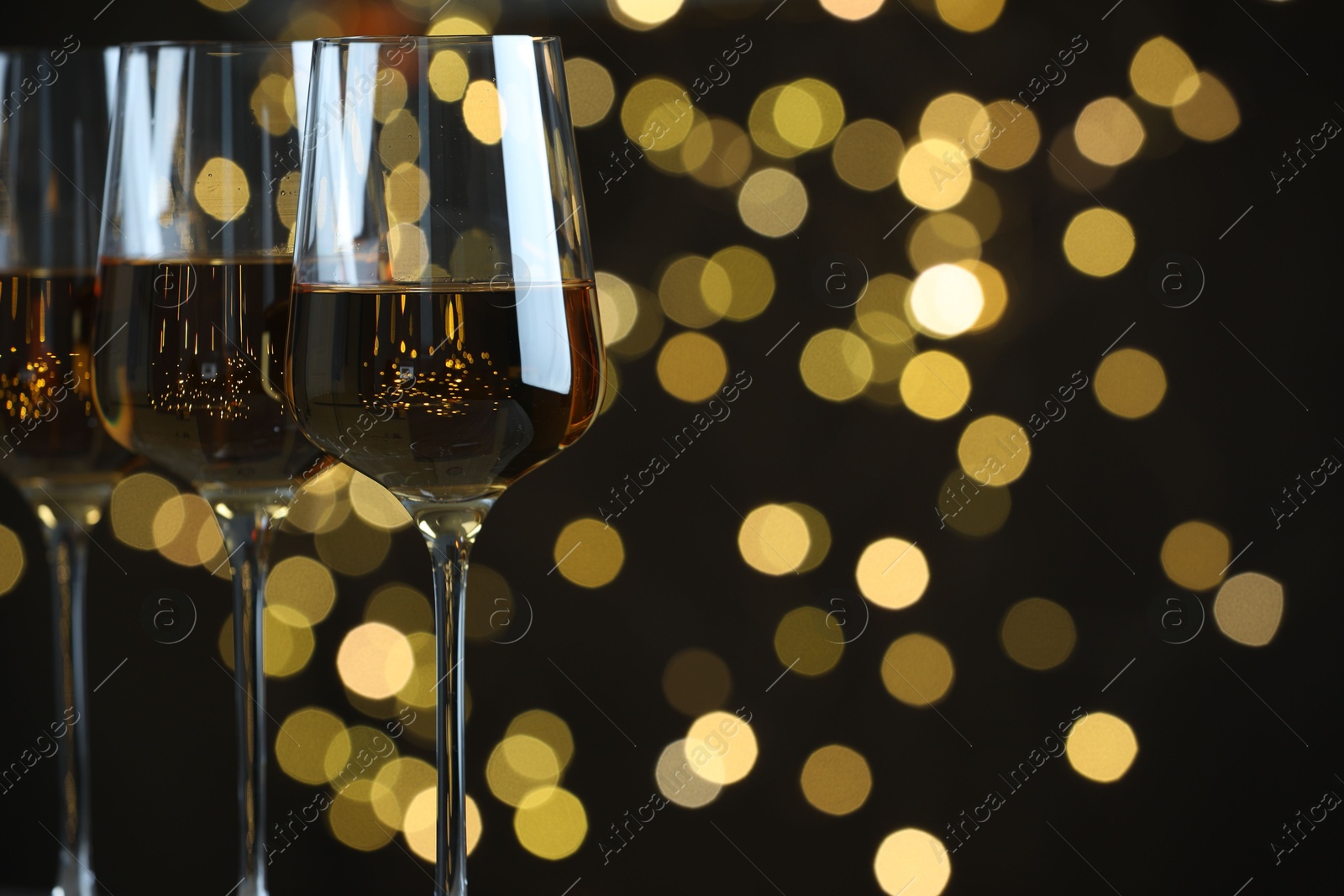 Photo of Glasses of luxury white wine against blurred lights, closeup. Bokeh effect